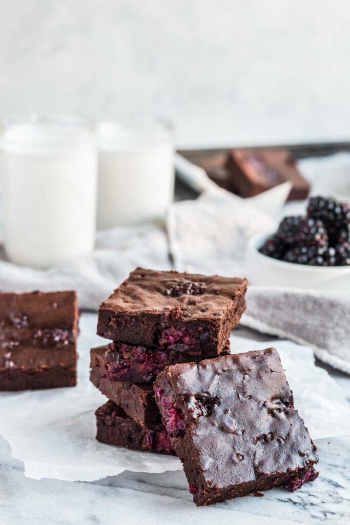 side angle of stacked blackberry brownies on marble surface with glasses of milk in background
