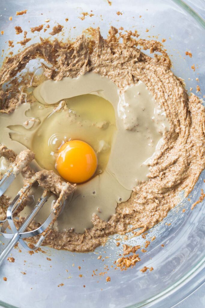 top down view of eggs and batter being mixed together in a mixing bowl for monster cookies