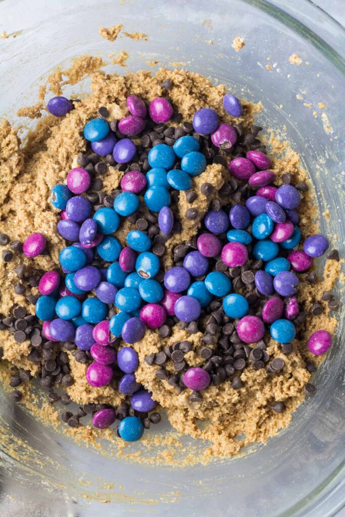 top down view of gluten-free monster cookie dough in a mixing bowl with colorful candy gems on top