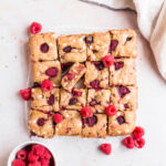 top down view of baked white chocolate raspberry blondies arranged in a square on a marble backdrop