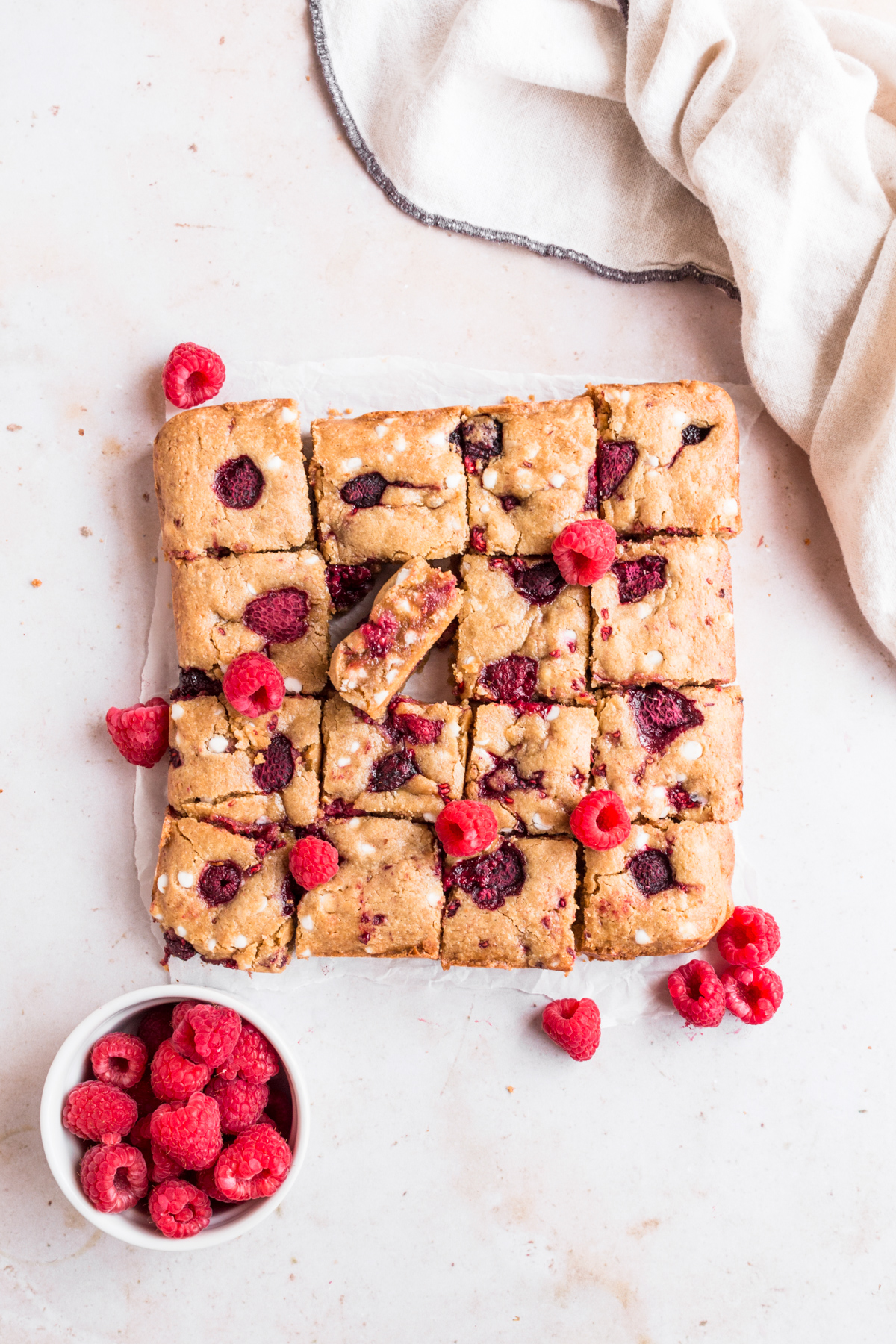 top down view of white chocolate raspberry blondies arranged in a square on a marble backdrop