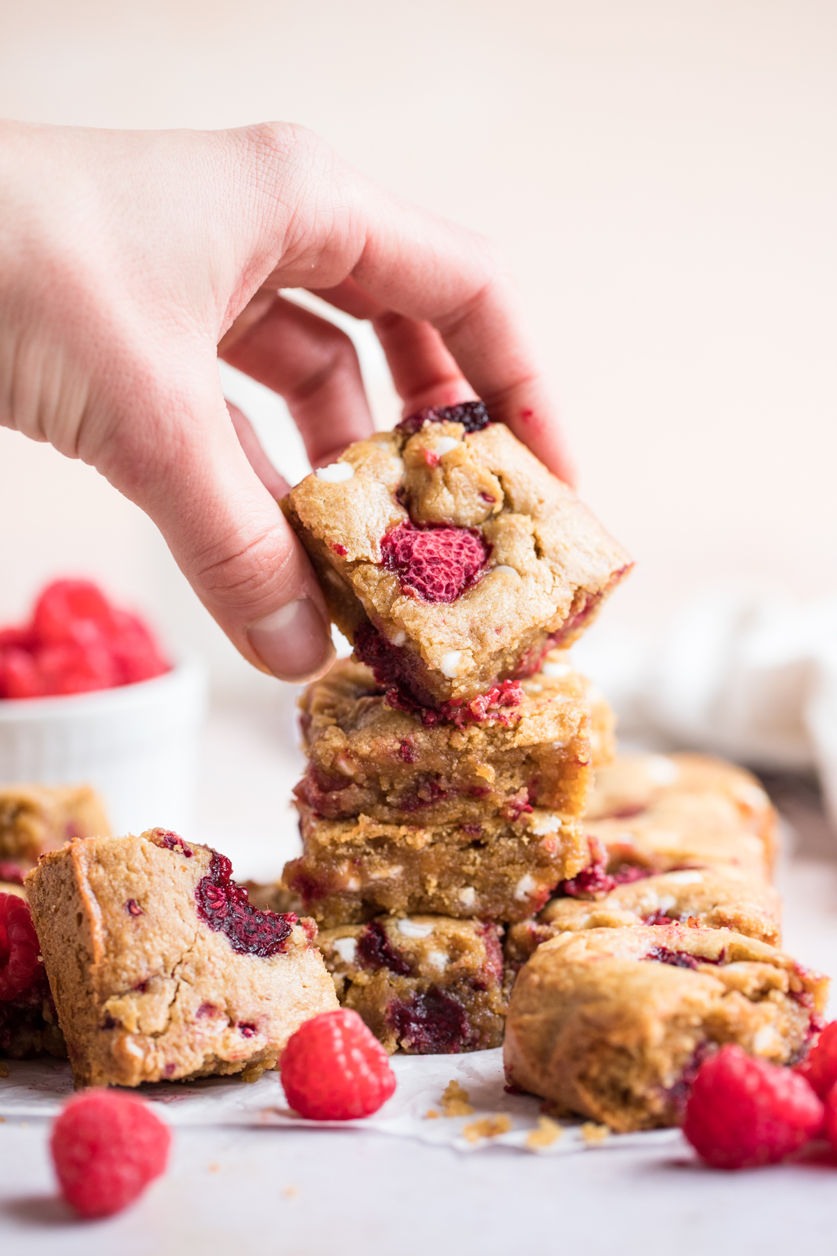 side view of stacked raspberry blondies - a hand is holding the top blondie square toward the camera