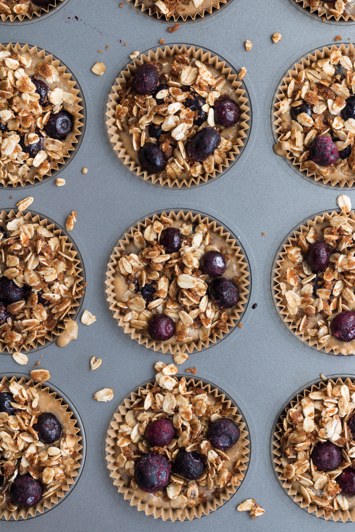 top down view of banana blueberry oatmeal muffin batter in lined muffin tin with oat topping and blueberries on top