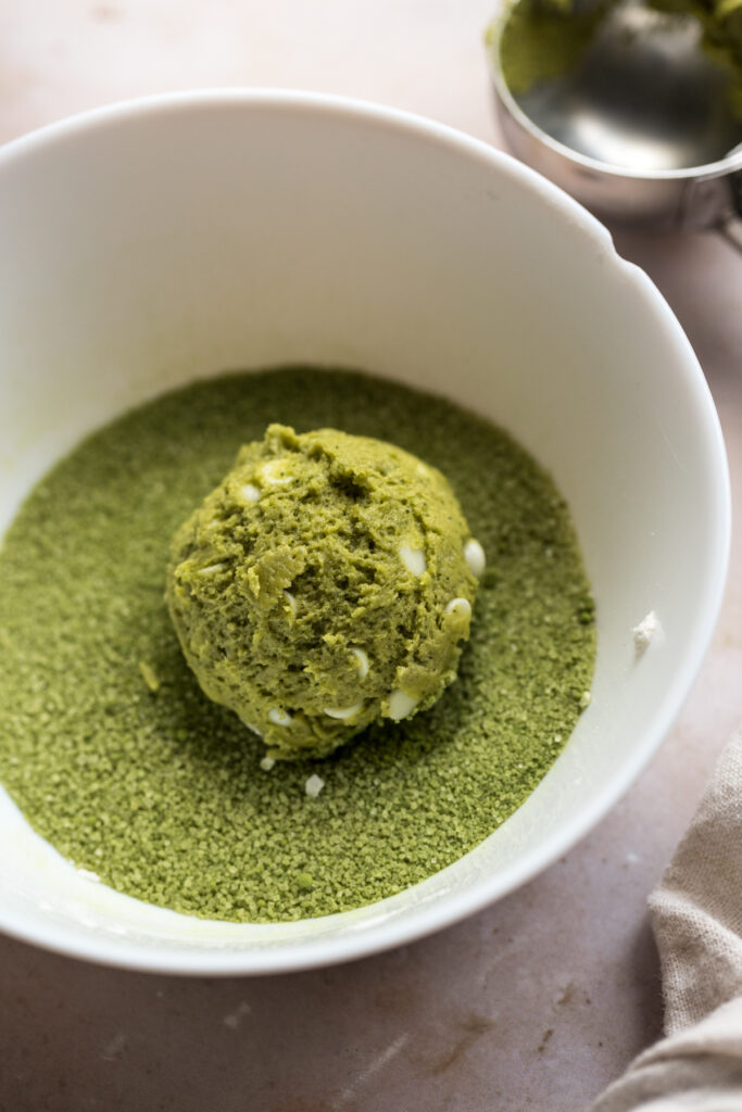 close up of matcha cookie dough ball being rolled in matcha sugar