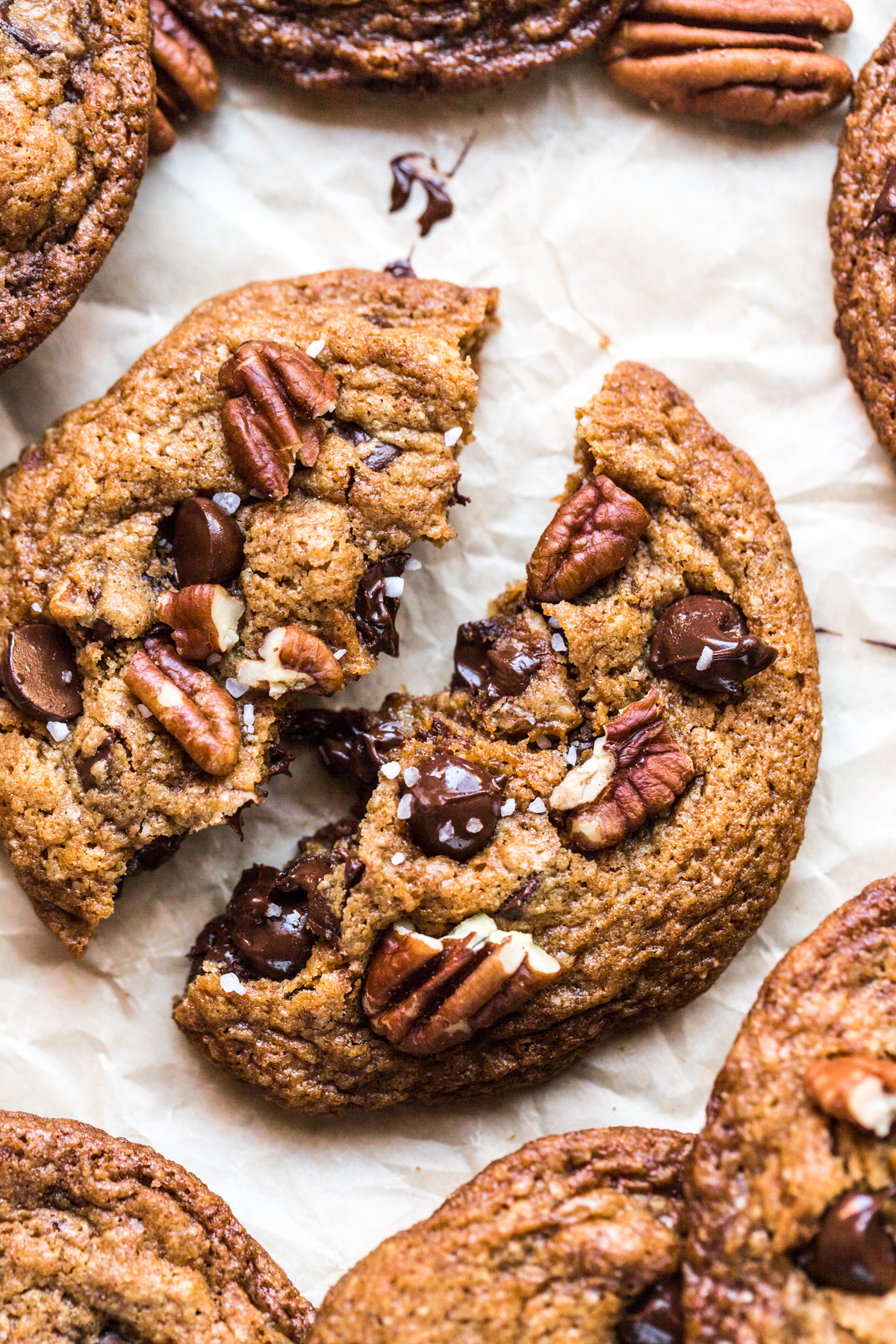 close up shot of pecan chocolate chip cookie broken in half on parchment paper background